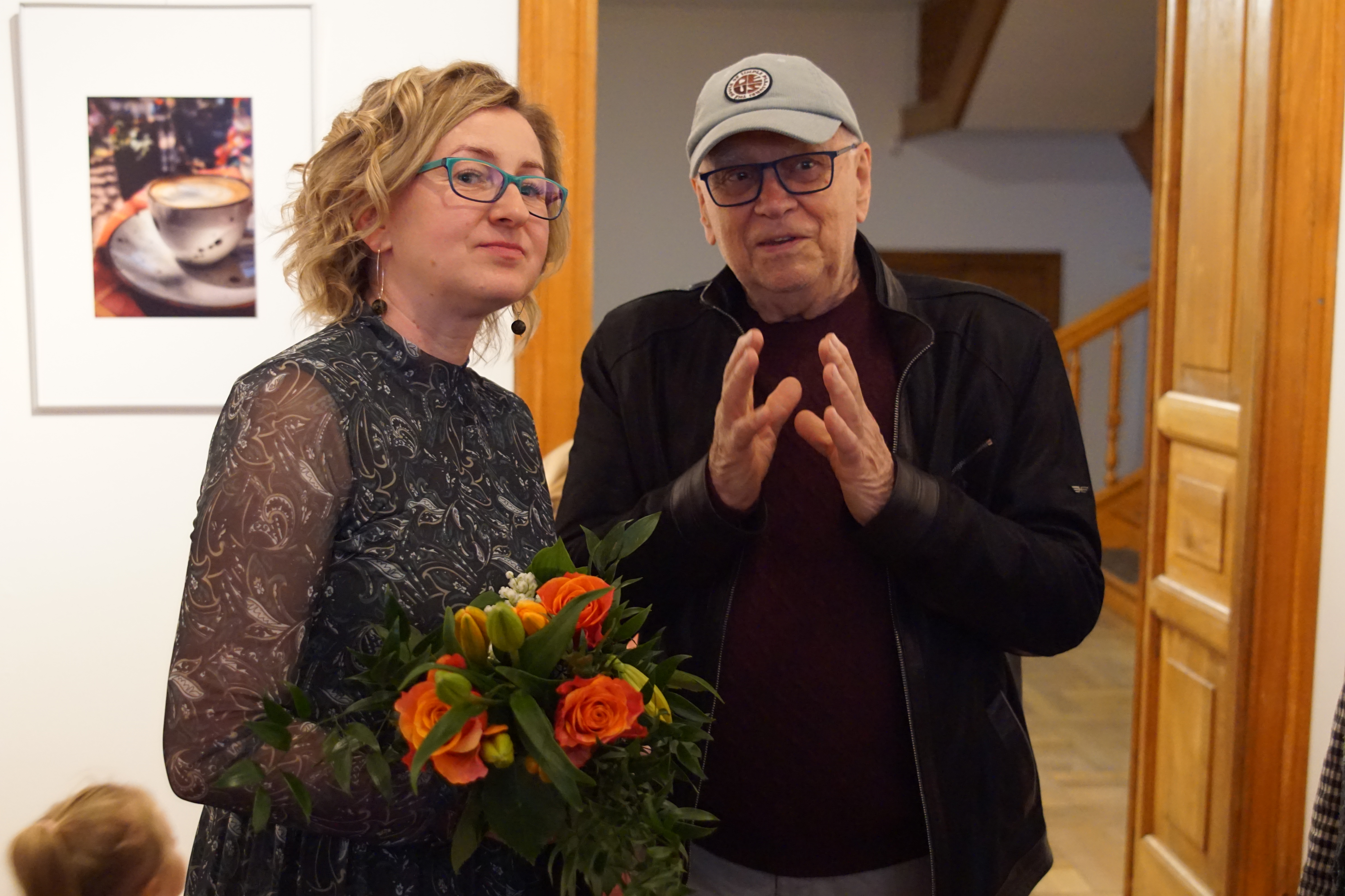 Monia Frys-Żurek z bukietem kwiatów rozmawia z mężczyzną w czapce z daszkiem.